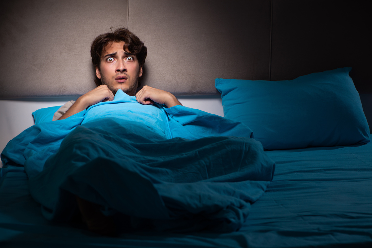 Homem deitado em cama assustado com pesadelo