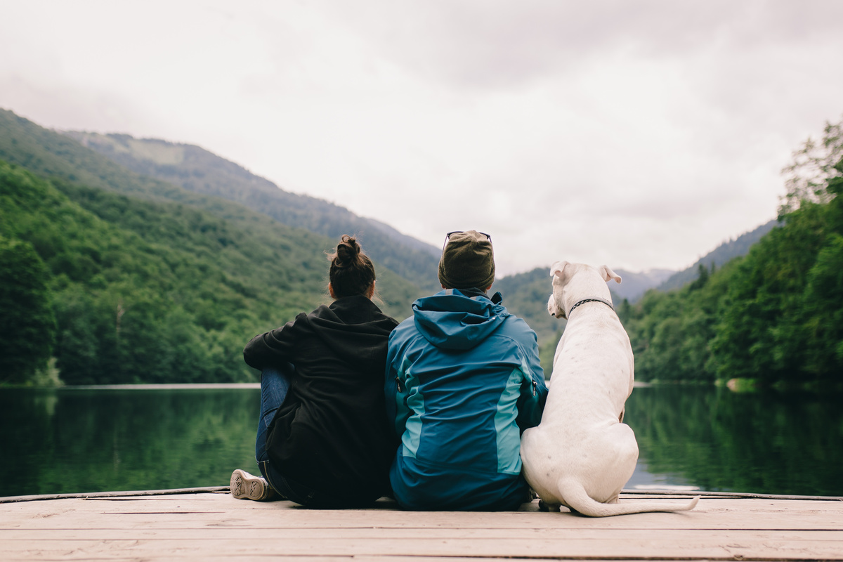 Casal sentado olhando para o lago e o cachorro sentado ao lado